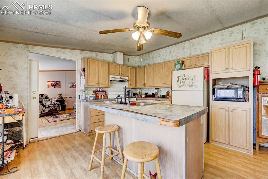 Image 10 of 44: Kitchen featuring wallpapered walls, a ceiling fan, a center island with si