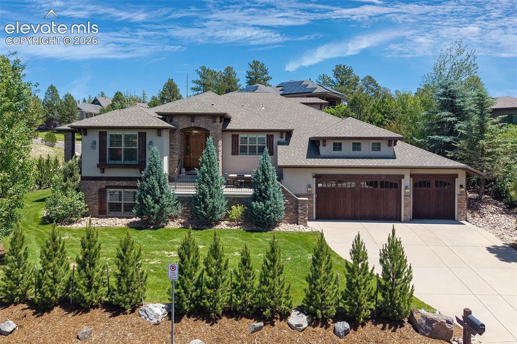 Caption: Stucco and stone facade with a multi-gabled roofline and dark wood-finish garage doors
