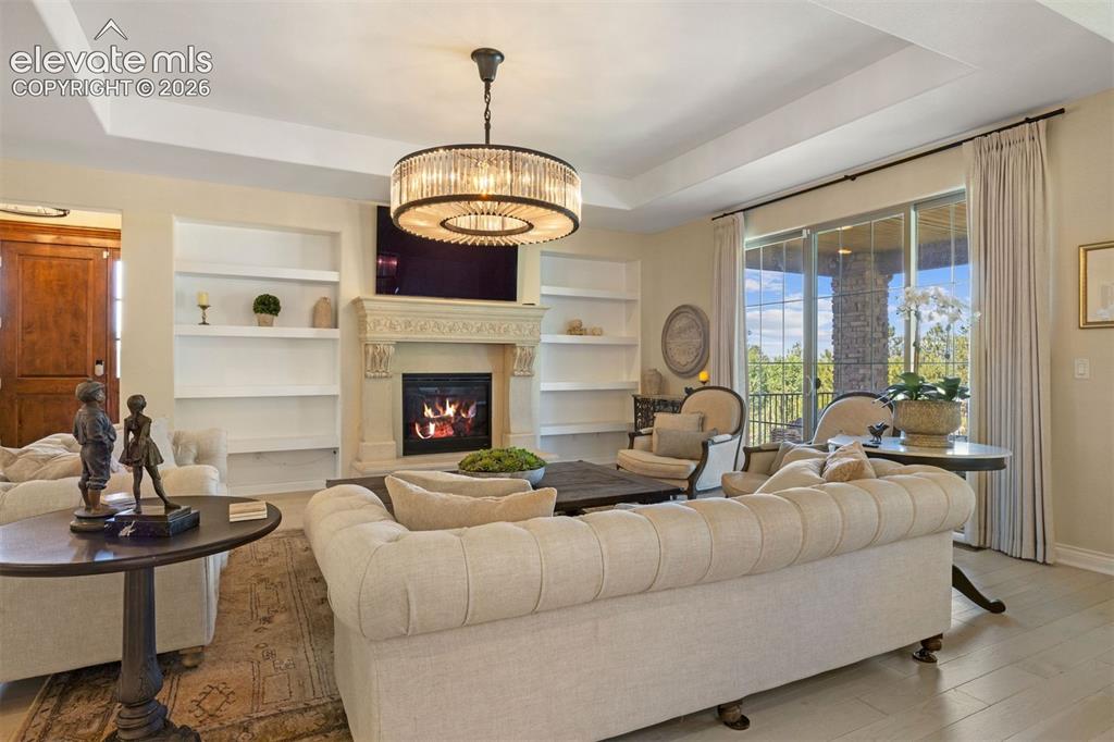 Image 5 of 49: Living area featuring a coffered ceiling, a decorative chandelier, a firepl