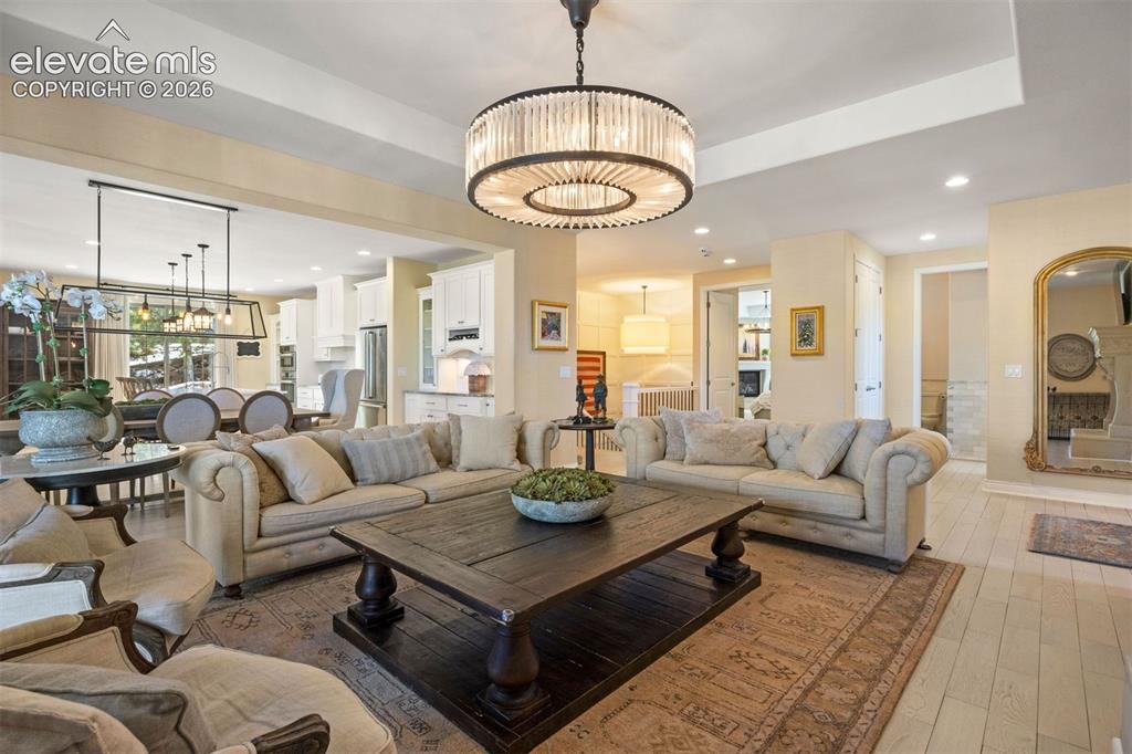 Image 6 of 49: Spacious living area featuring a large central chandelier, wood-finish floo