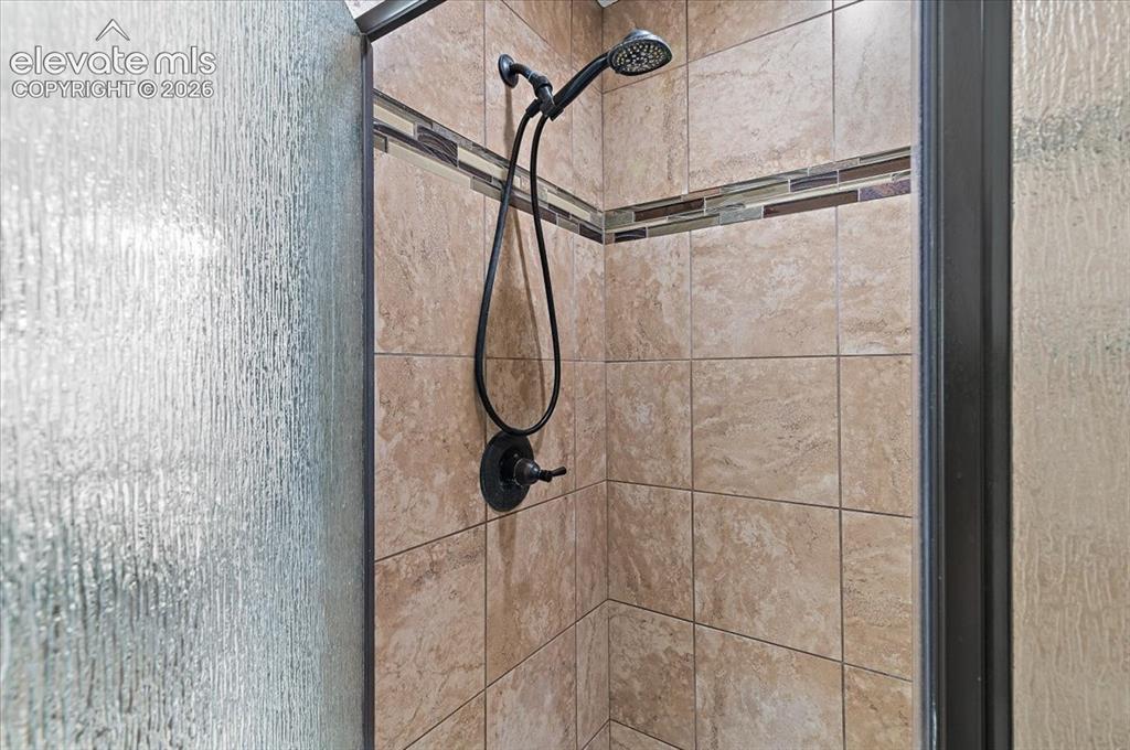 Image 16 of 39: Shower enclosure featuring textured glass, neutral-toned tile, decorative t