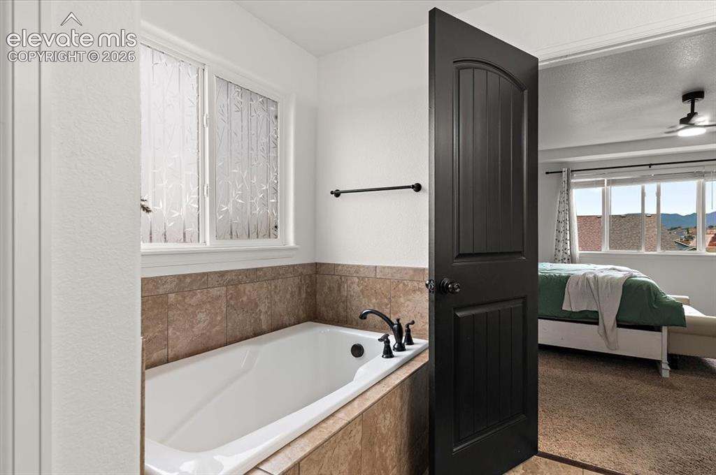 Image 17 of 39: Built-in bathtub with tiled surround, white window with privacy glass, and
