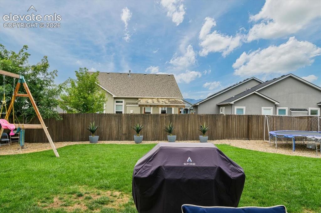 Image 32 of 39: Fenced backyard featuring a manicured lawn, gravel accents, and mature plan