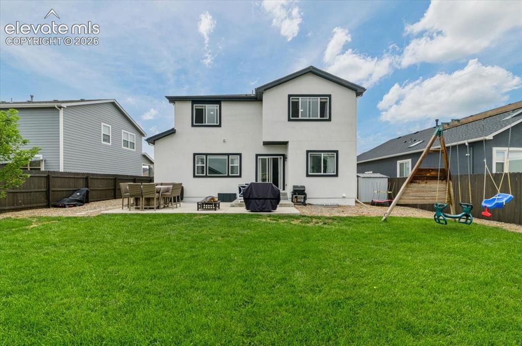 Image 33 of 39: Expansive green lawn with a privacy fence, two-story exterior, and a patio