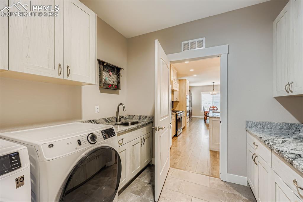 Image 35 of 42: Well-appointed laundry/mudroom with built-in cabinetry, utility sink, and d
