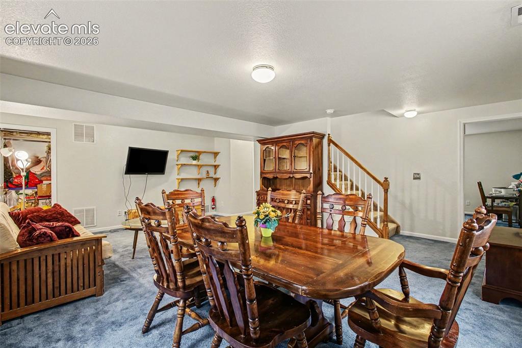 Image 21 of 33: Spacious room with blue carpeting, a wooden staircase with white risers and