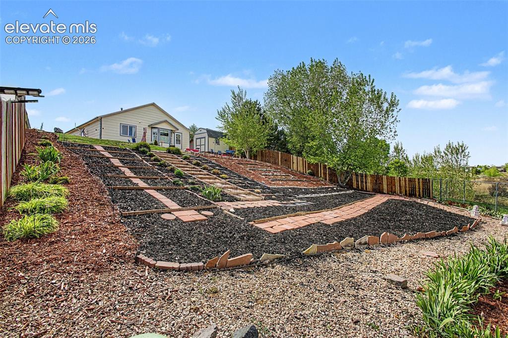 Image 28 of 33: Terraced backyard landscaping featuring brick pathways and planting beds