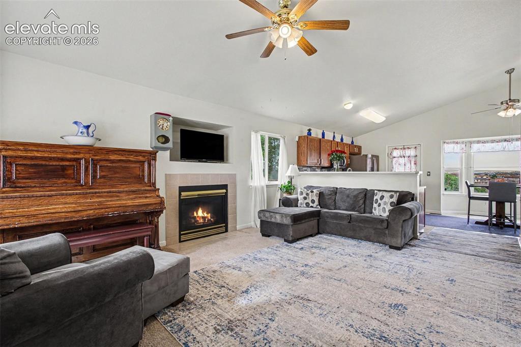 Image 4 of 33: Living area with a vaulted ceiling, ceiling fan, and a fireplace featuring 