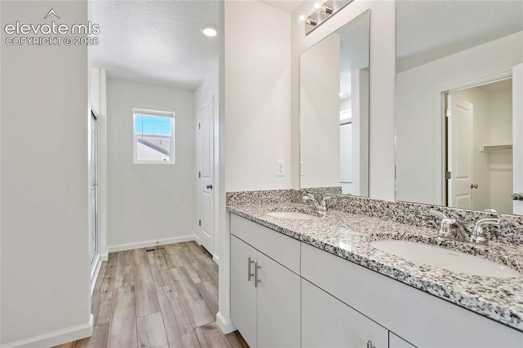 Image 12 of 25: Dual vanity with granite-style countertop, white cabinetry, and undermount 