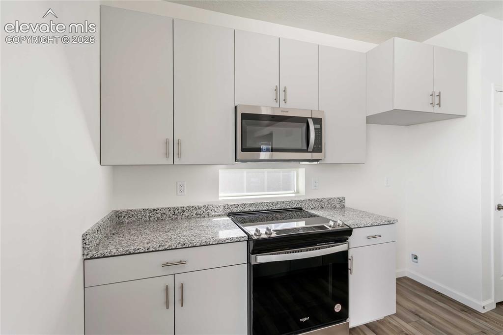 Image 8 of 25: Light gray cabinetry, speckled countertops, stainless steel microwave, and