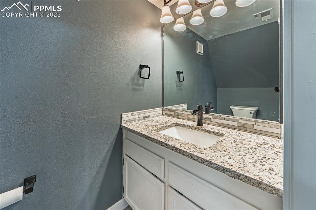 Image 10 of 46: Half bathroom featuring a textured wall, vanity, and backsplash