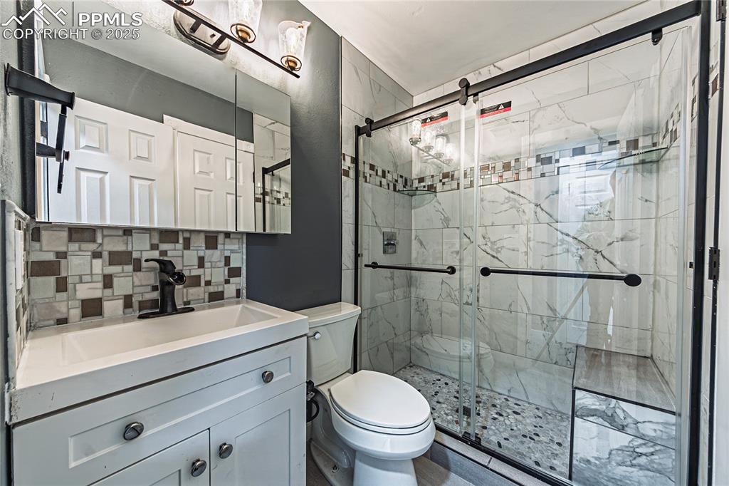 Image 17 of 46: Full bath featuring backsplash, vanity, and a marble finish shower
