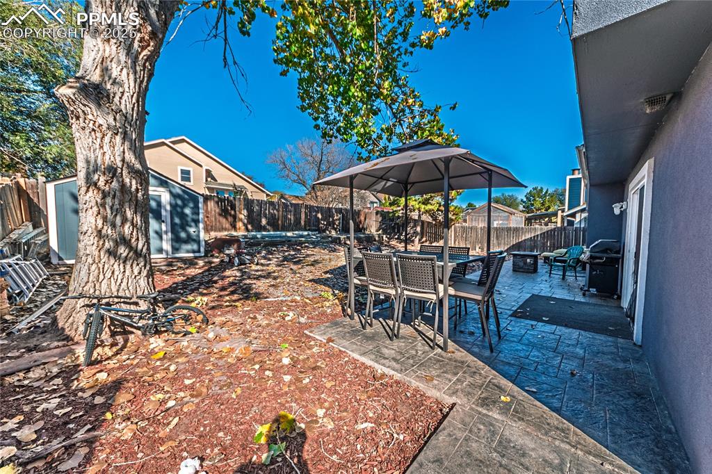Image 28 of 46: Fenced backyard with a patio area, outdoor dining area, a storage shed, and