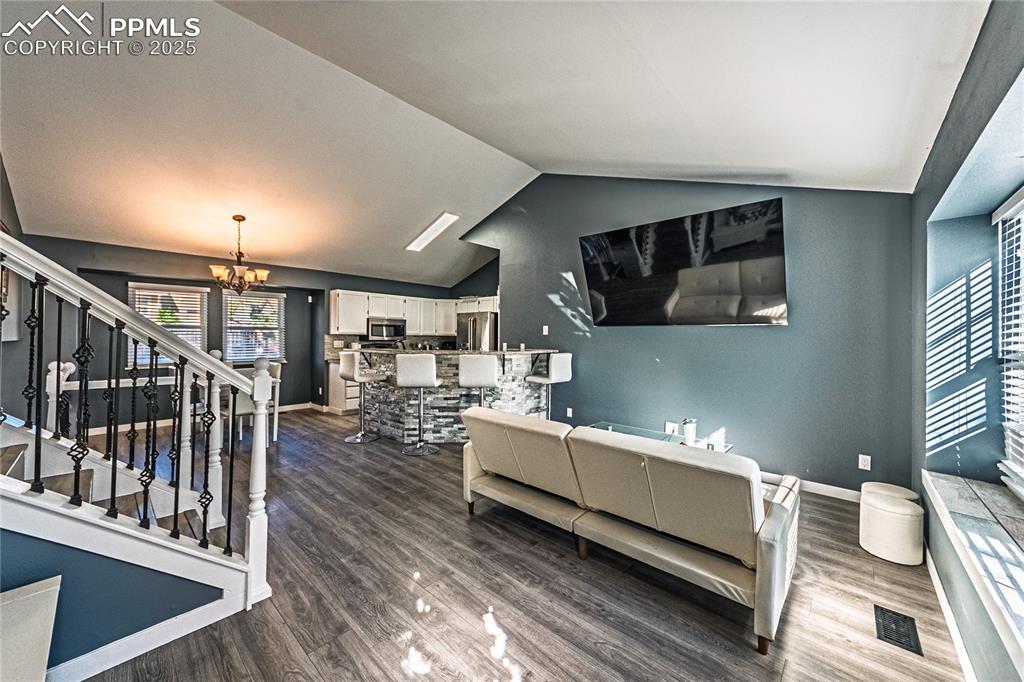 Image 3 of 46: Living area with a chandelier, dark wood finished floors, stairs, and vault