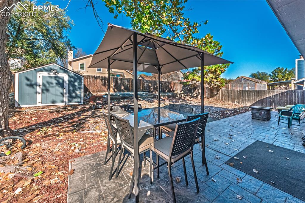 Image 30 of 46: Fenced backyard with outdoor dining area, an outdoor fire pit, a storage sh