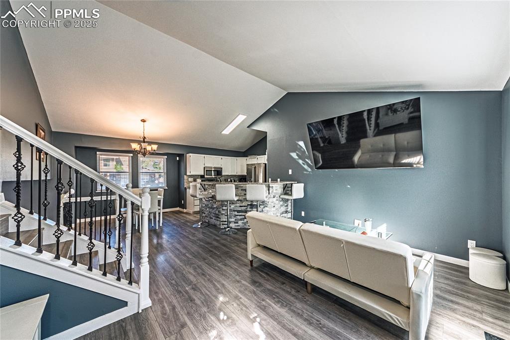 Image 4 of 46: Living area with stairway, dark wood-style floors, a chandelier, and vaulte