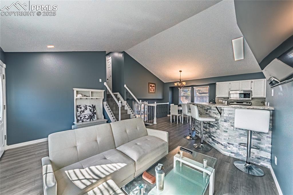 Image 6 of 46: Living area with a chandelier, vaulted ceiling, dark wood-style floors, a t