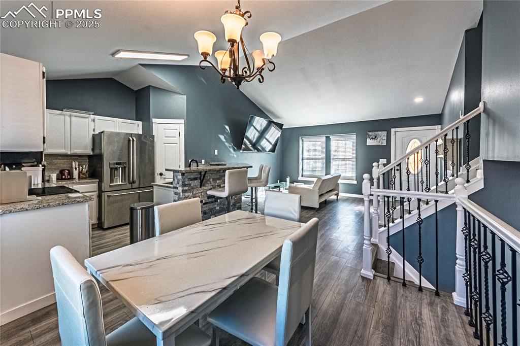 Image 9 of 46: Dining area featuring vaulted ceiling, a chandelier, dark wood-style floors