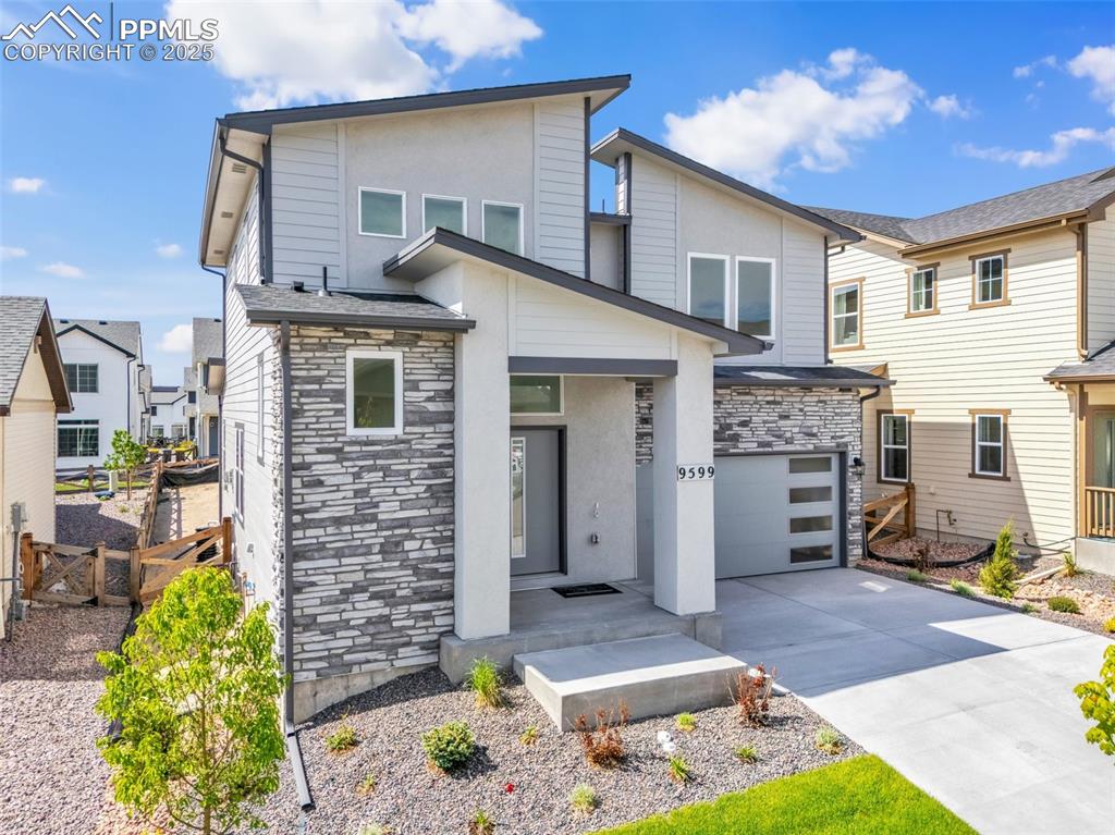 Image 2 of 43: Contemporary home featuring stone siding, concrete driveway, an attached ga
