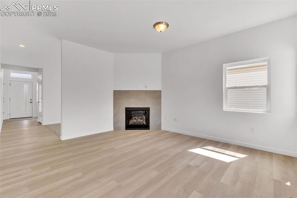 Image 25 of 43: Unfurnished living room with a tile fireplace and light wood-style flooring