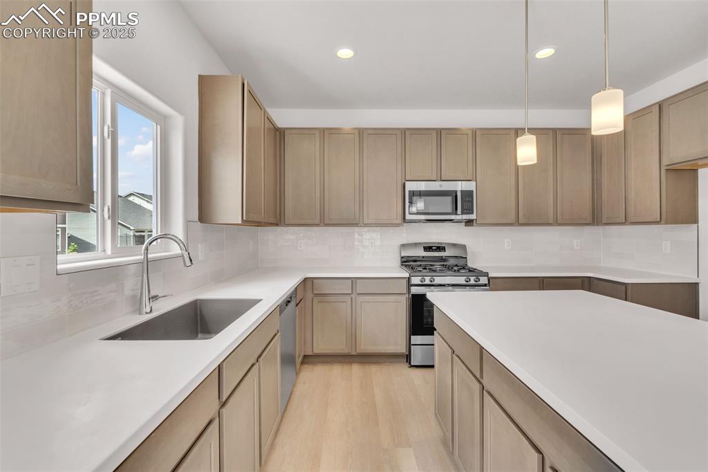 Image 33 of 43: Kitchen featuring stainless steel appliances, backsplash, decorative light 