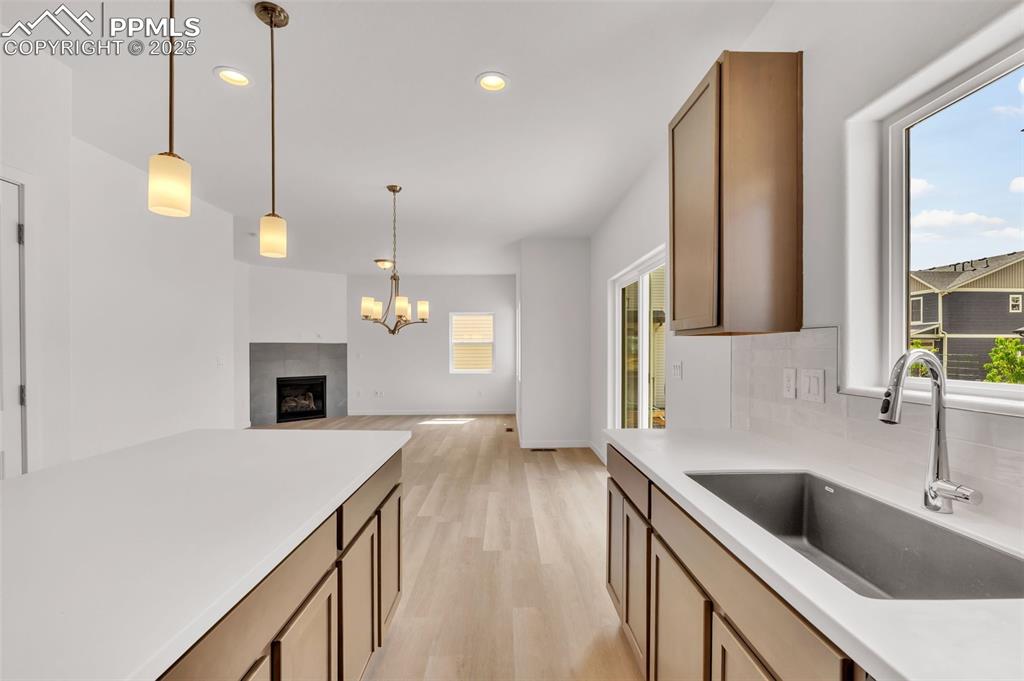 Image 35 of 43: Kitchen with a tiled fireplace, light wood-style flooring, decorative light