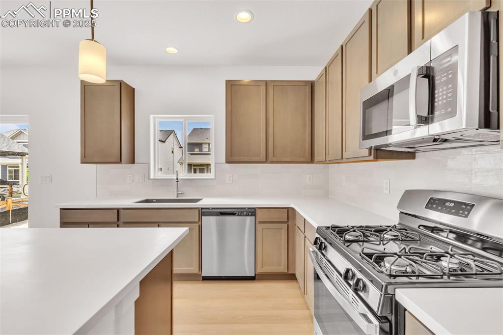 Image 37 of 43: Kitchen with stainless steel appliances, decorative backsplash, pendant lig