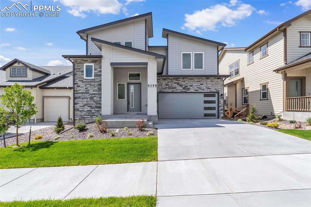 Image 5 of 43: Modern home with stone siding, concrete driveway, a front yard, an attached