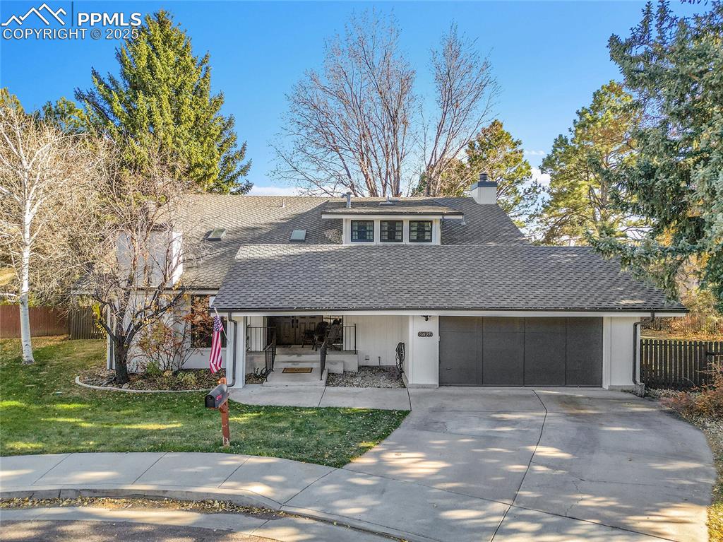 Caption: Mid-century home featuring covered porch, a shingled roof, concrete driveway, a chimney, and a garag