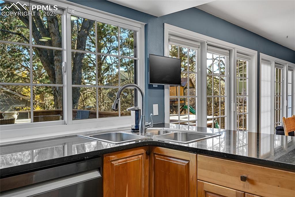 Image 13 of 43: Kitchen featuring dark stone counters, brown cabinetry, and dishwasher