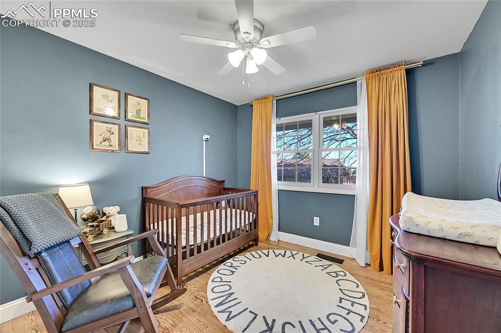 Image 29 of 43: Bedroom with a nursery area, light wood-style floors, and a ceiling fan