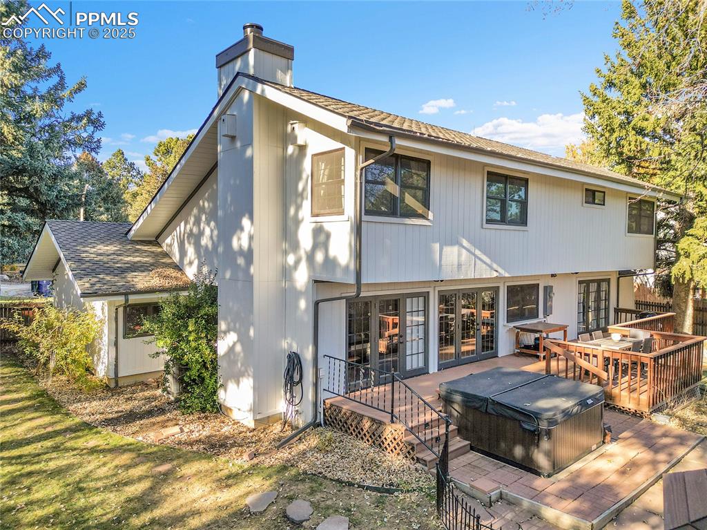 Image 36 of 43: Rear view of house with a hot tub, french doors, a chimney, and a wooden de