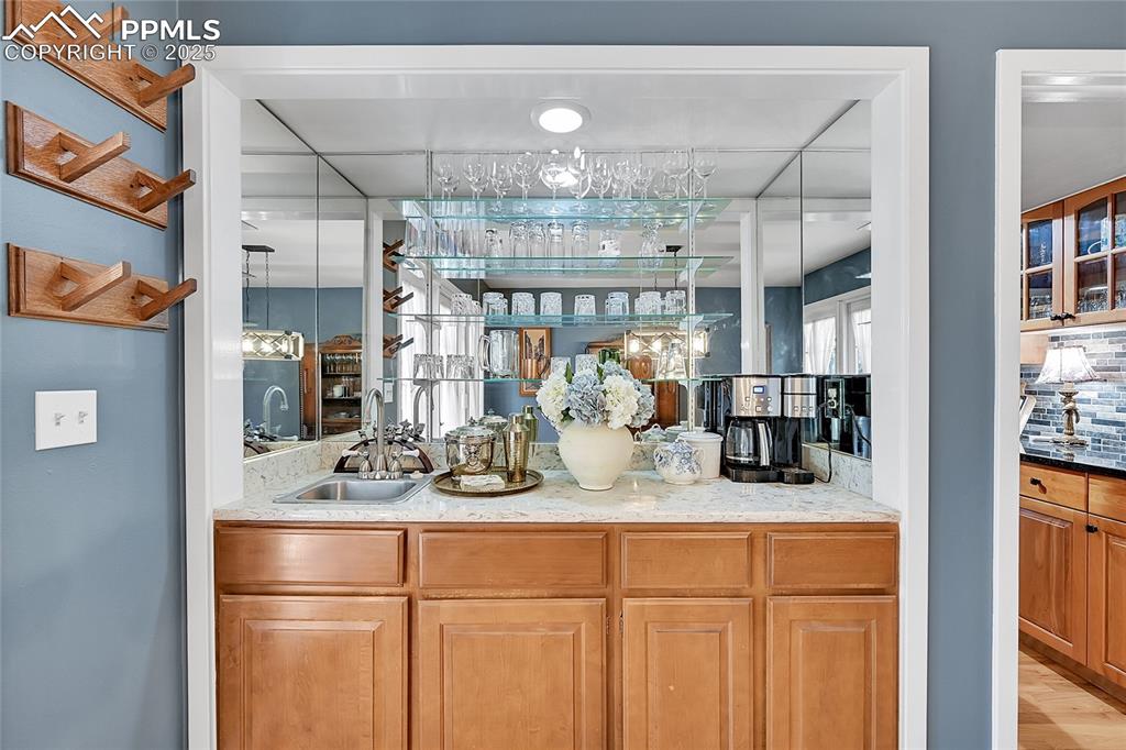 Image 9 of 43: Indoor wet bar with light stone counters, brown cabinetry, and glass insert