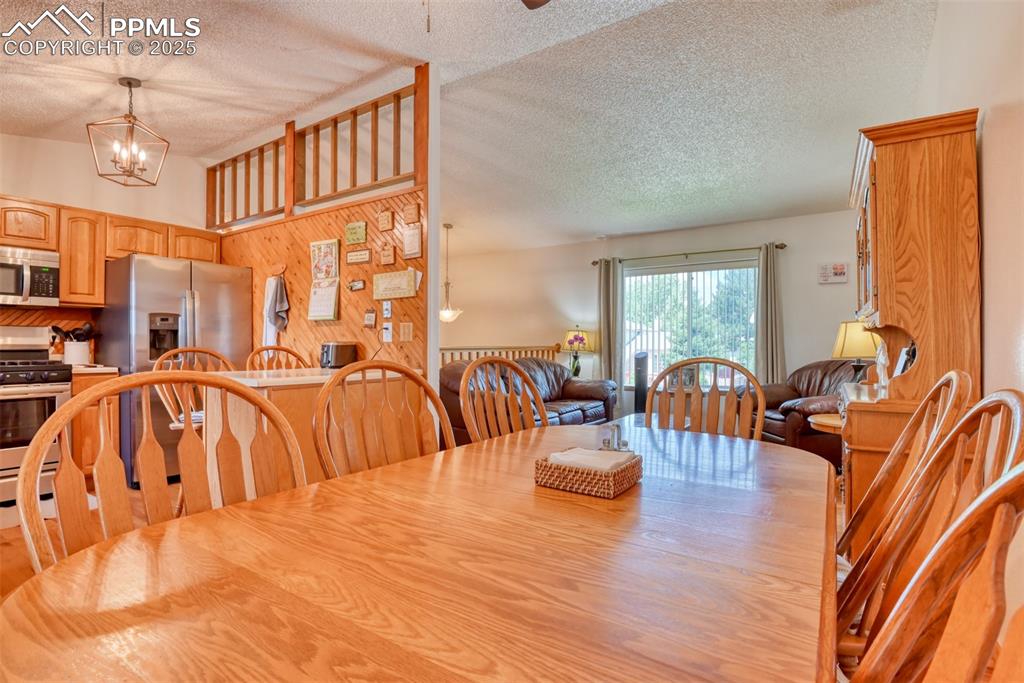 Image 11 of 46: Dining room with a textured ceiling, a chandelier, ceiling fan, and wood wa
