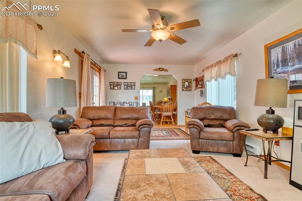 Image 28 of 46: Living room featuring arched walkways, ceiling fan, light carpet, and baseb