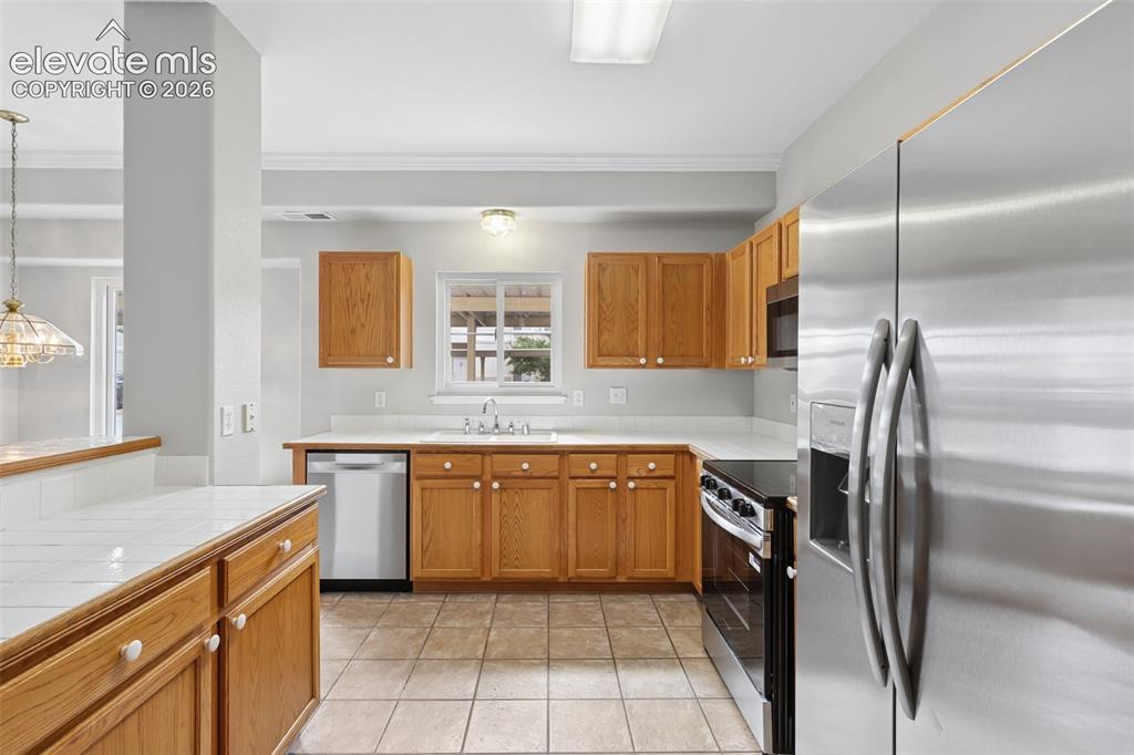 Image 10 of 27: Kitchen featuring wood cabinetry, stainless steel appliances, tile flooring