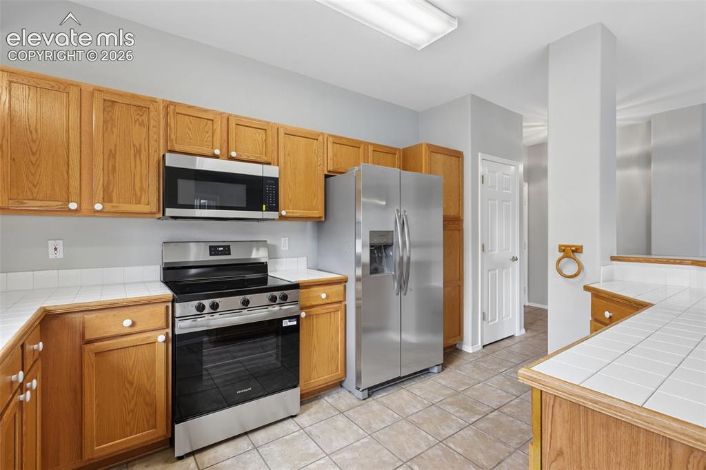 Image 11 of 27: Wood-finish cabinetry, stainless steel appliances, tile flooring, and a til