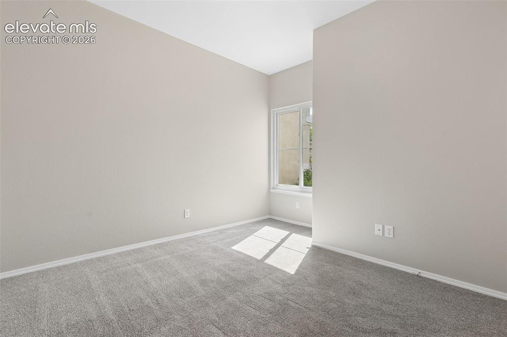 Image 19 of 27: Neutral tone walls, grey carpet flooring, and a single window with white tr