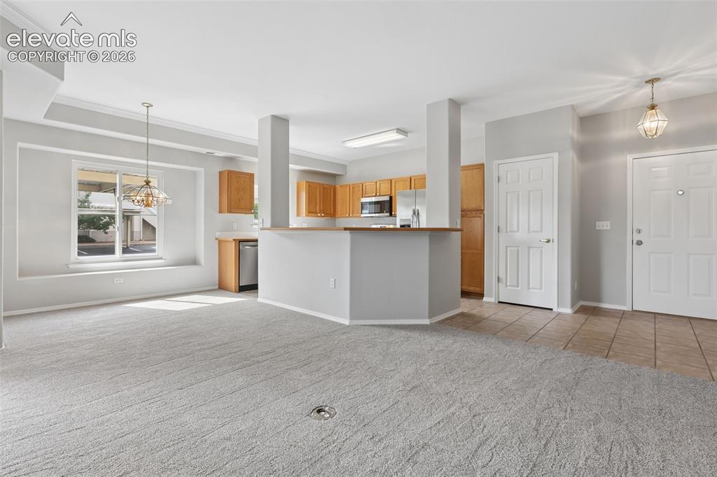 Image 5 of 27: Open-concept living area with carpet flooring, a kitchen featuring wood cab