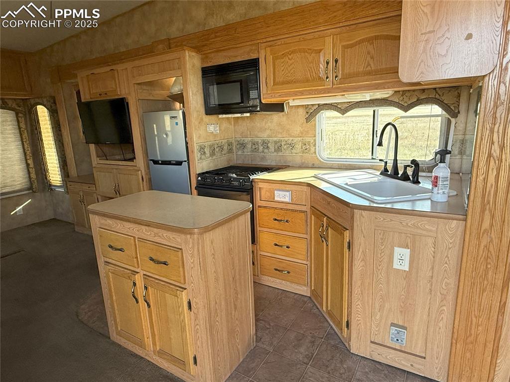 Image 9 of 15: Kitchen featuring light countertops, black appliances, and a kitchen island