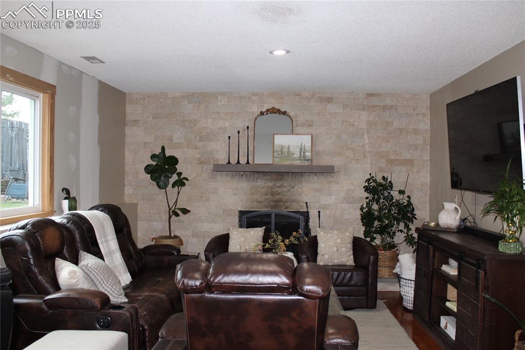 Image 11 of 26: Living area with a large fireplace, wood finished floors, and a textured ce