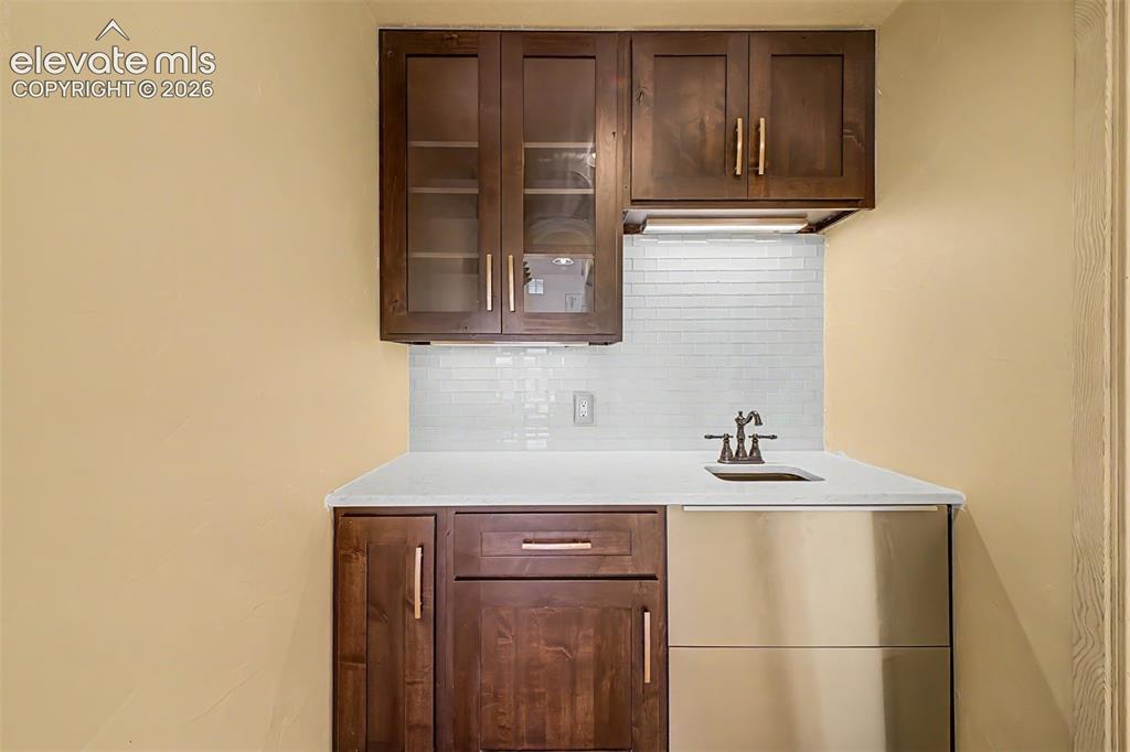 Image 19 of 50: Wet bar featuring wood-finish cabinetry, glass-front upper cabinets, a whit