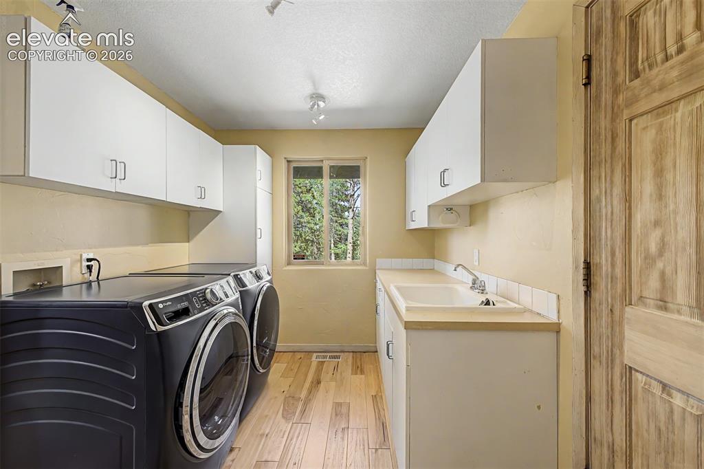 Image 20 of 50: Utility room featuring wood-finish flooring, white cabinetry, a utility sin