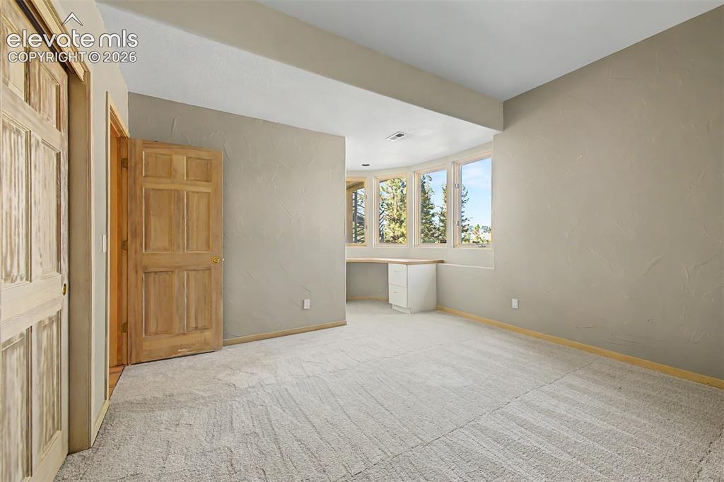Image 32 of 50: Carpeted room with a built-in desk, bay windows, and wood panel doors