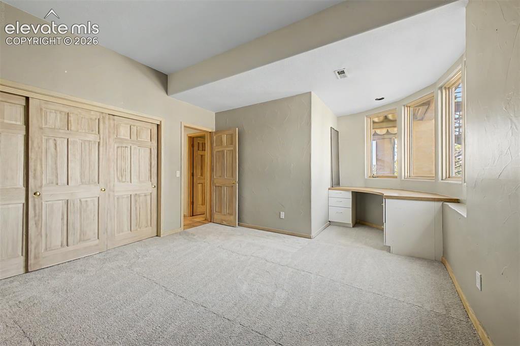 Image 33 of 50: Built-in desk with a curved window wall, neutral carpeting, and panel-style
