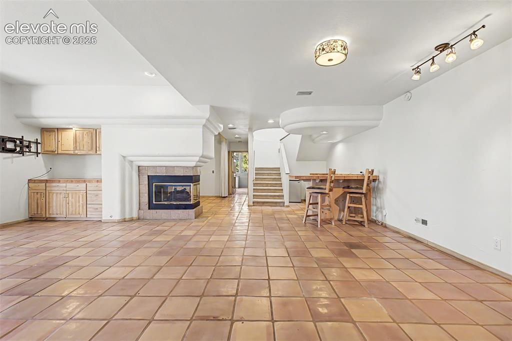 Image 35 of 50: Terracotta tile flooring, built-in wet bar cabinetry, corner fireplace with