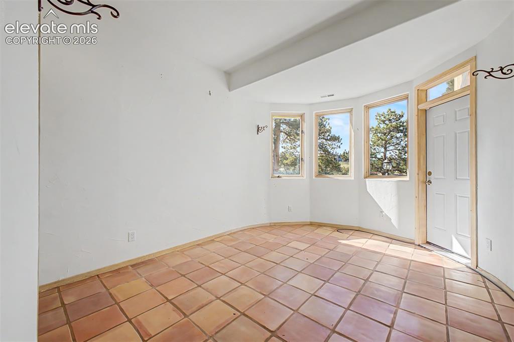 Image 44 of 50: Terracotta tile flooring, three large windows, white paneled door, and whit