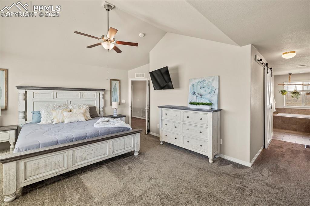 Image 16 of 36: Bedroom with visible vents, baseboards, a barn door, carpet, and vaulted ce
