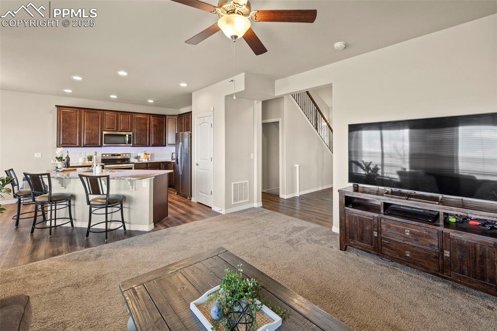 Image 9 of 36: Living area with a ceiling fan, baseboards, visible vents, and dark carpet