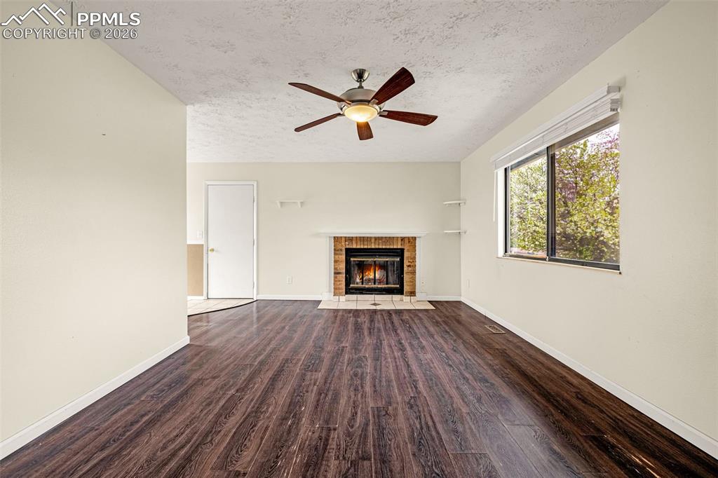 Image 3 of 21: Living room with wood-burning fireplace, ceiling fan, wood laminate floorin